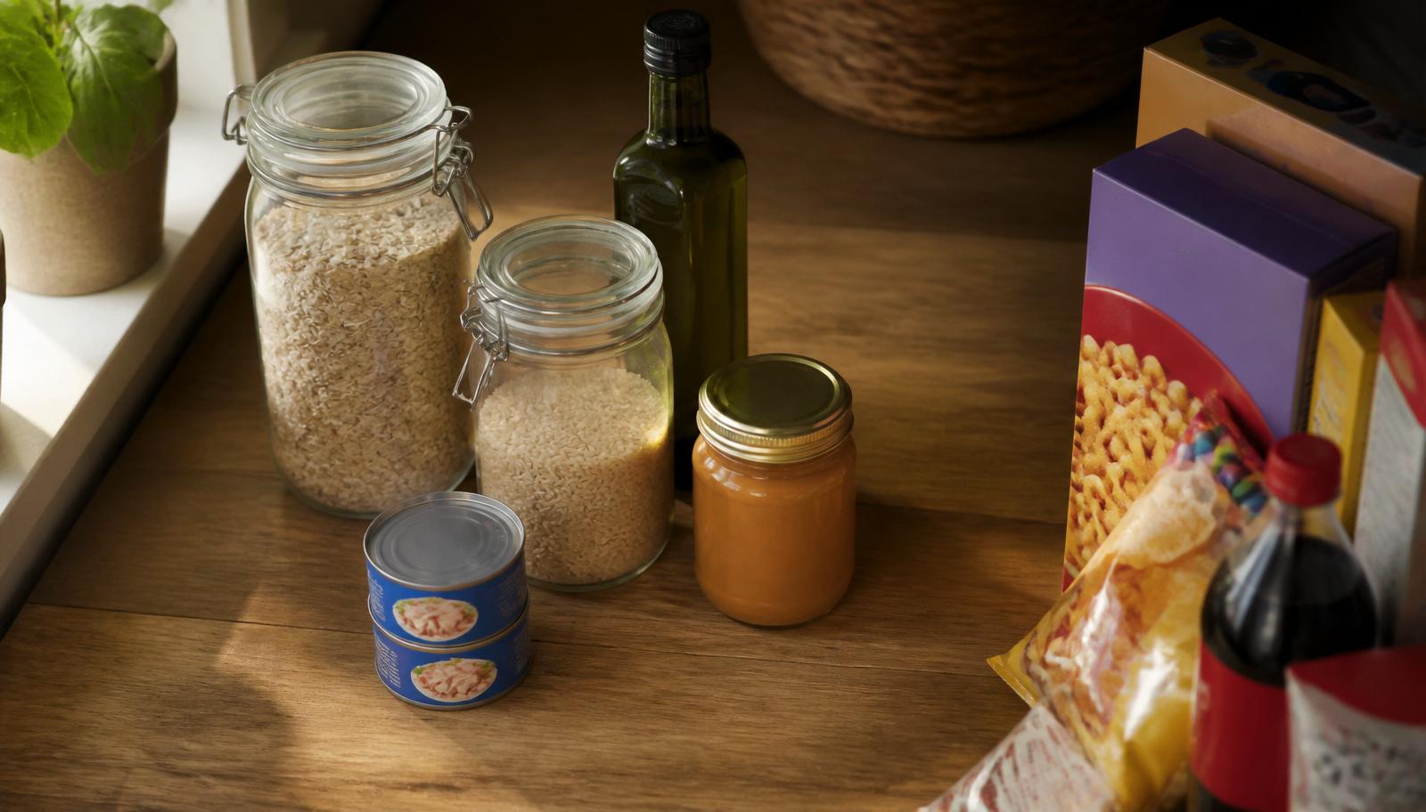 Home pantry mid cleanup: oats, brown rice, olive oil, and canned tuna staying while processed snack boxes and soda get pulled to the side.